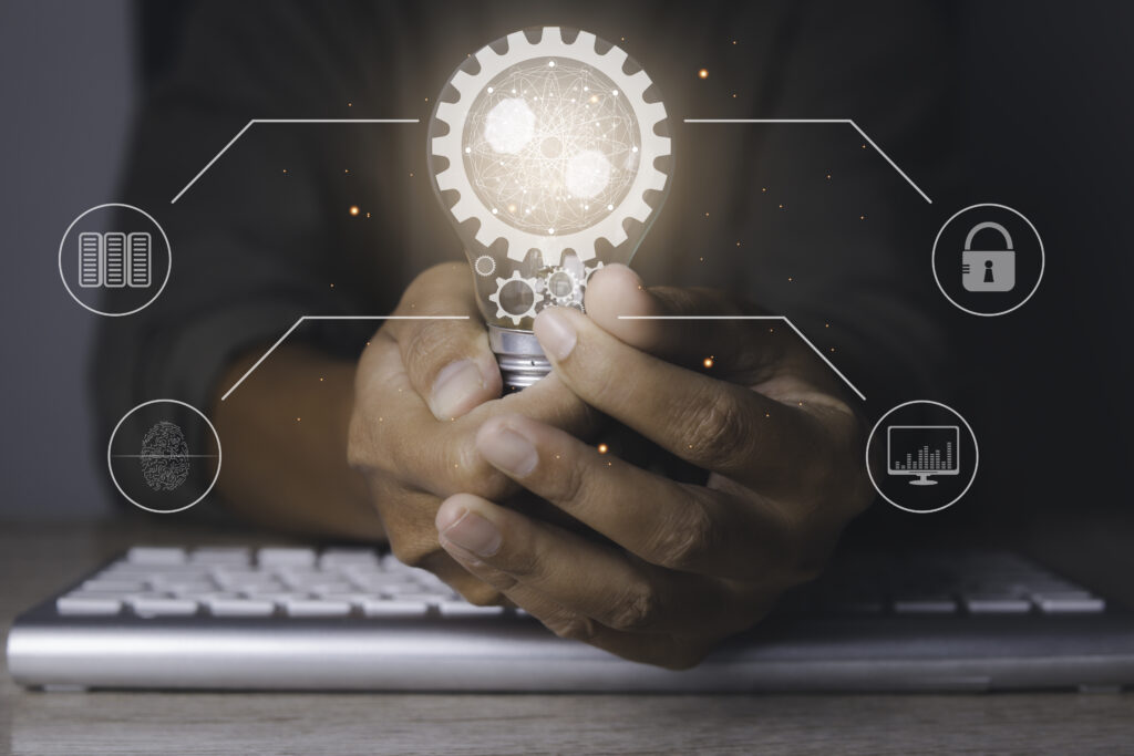 man holding a bright light bulb with gear icon and using laptop